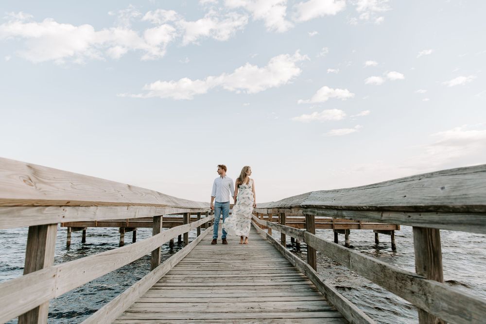 couple standing on a boardwalk holding hands and looking opposite directions of each other