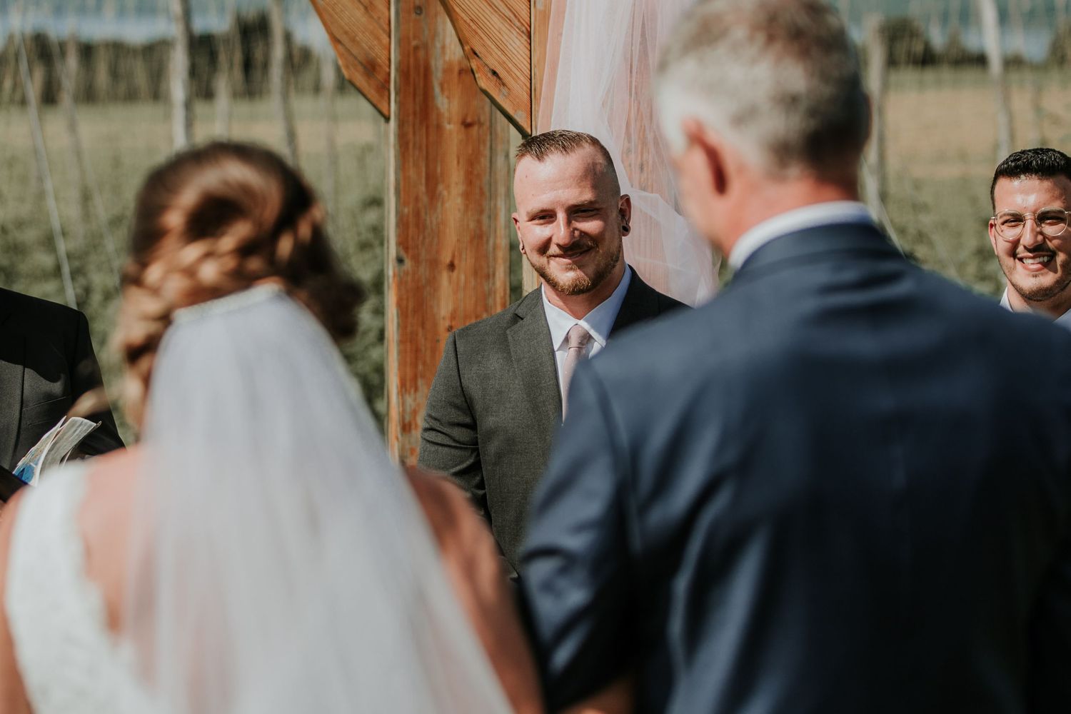 groom smiling at bride shot between the backs of bride and father of the bride