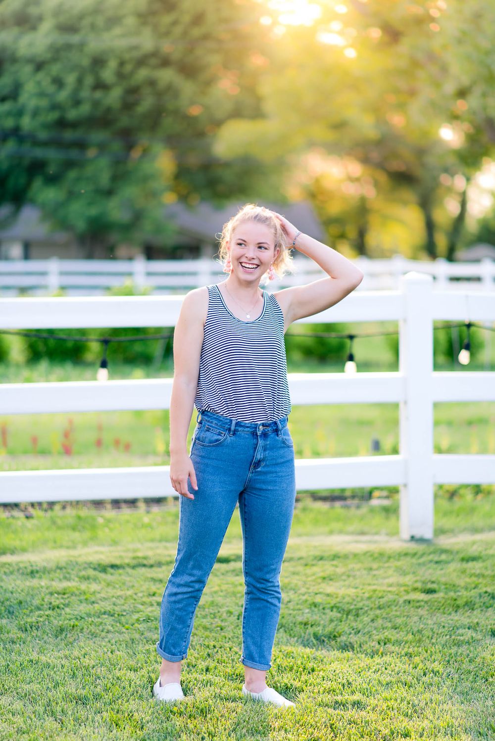 young woman in jeans and striped tank top holding her ponytail