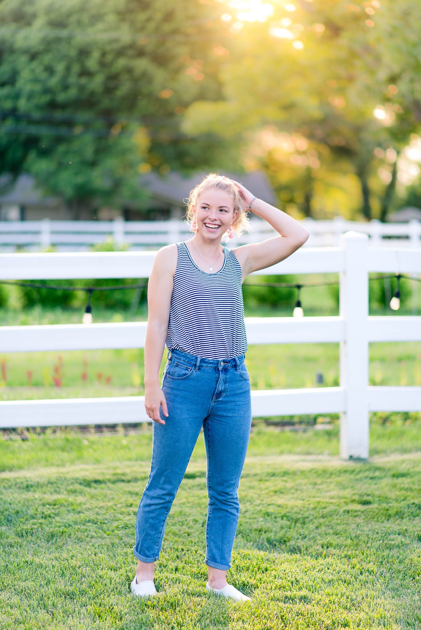 young woman in jeans and striped tank top holding her ponytail