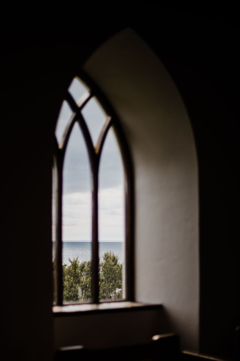 Gothic arched window in a church framing a serene ocean view.