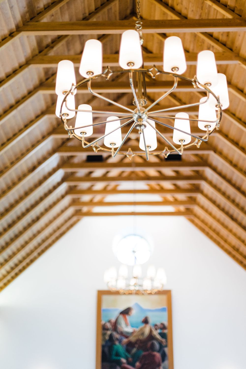 Elegant chandelier with white glass shades hanging from a wooden church ceiling.