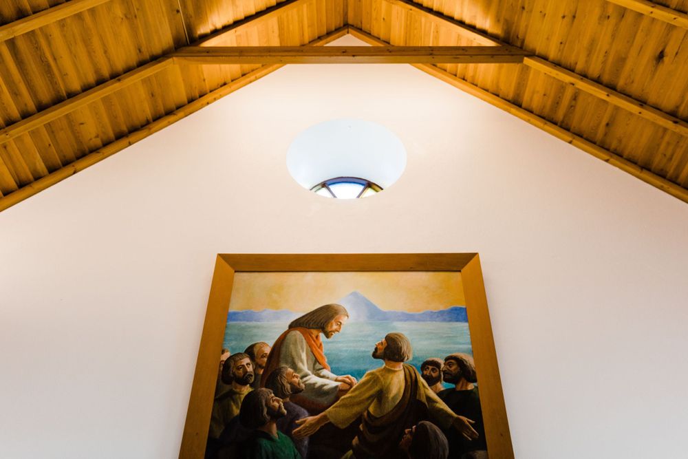 Religious painting illuminated beneath a vaulted wooden ceiling with exposed beams in a church.
