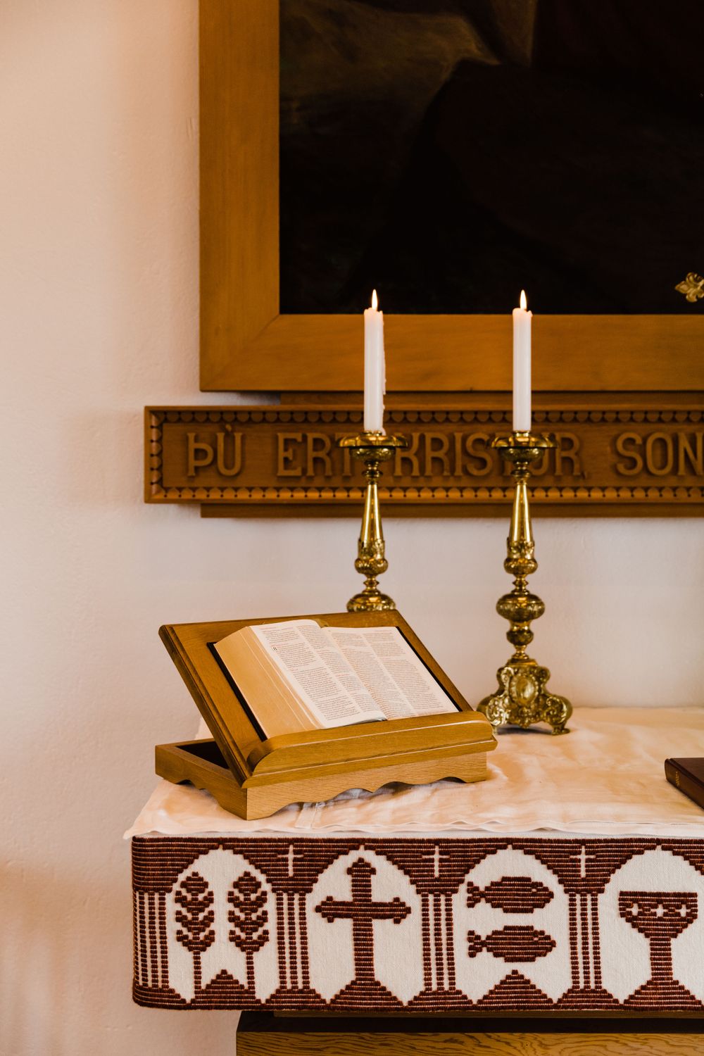 A church altar decorated with candles, a bible stand, and embroidered cloth with religious symbols.