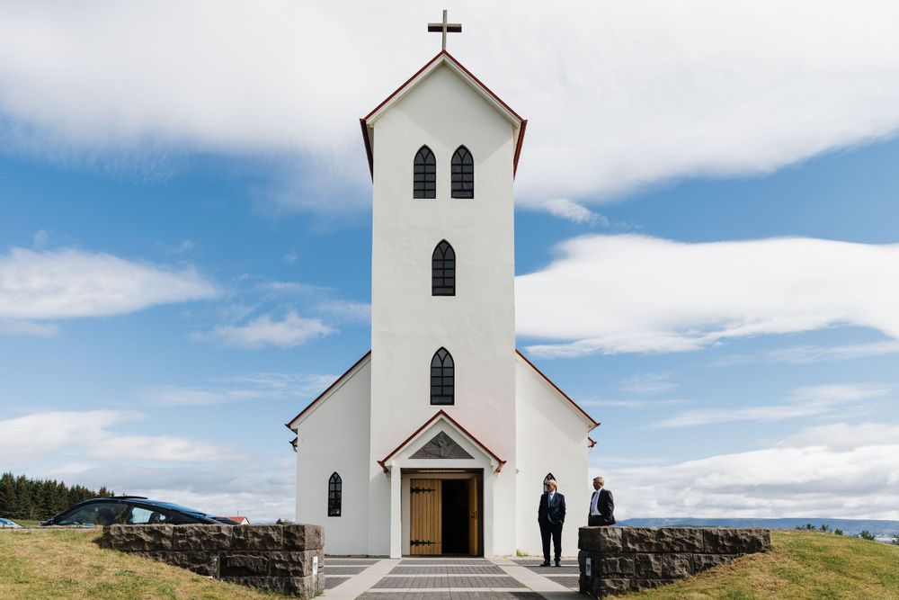 Simple white country church with tall steeple against blue sky and mountains.