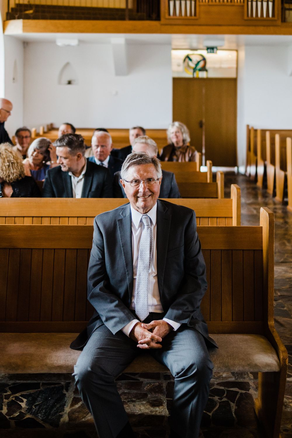 Wedding guest in a suit sits on wooden church pew during ceremony.