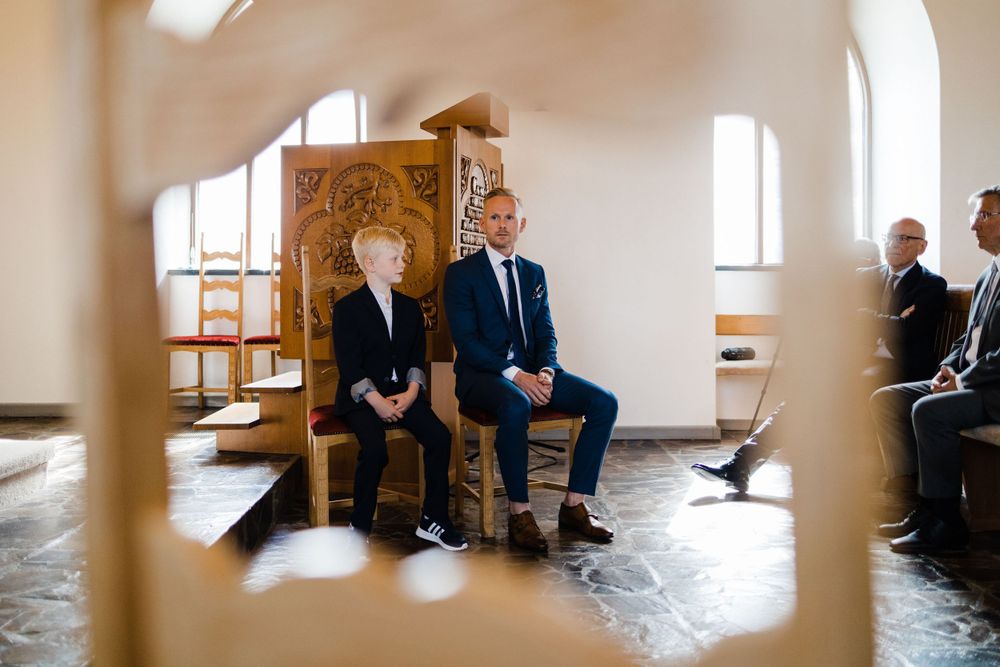 Two people sitting on ornate wooden chairs during a wedding ceremony in a church.