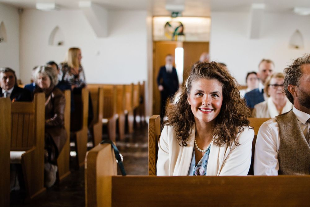 Wedding guest seated in a wooden church pew smiles during the ceremony.