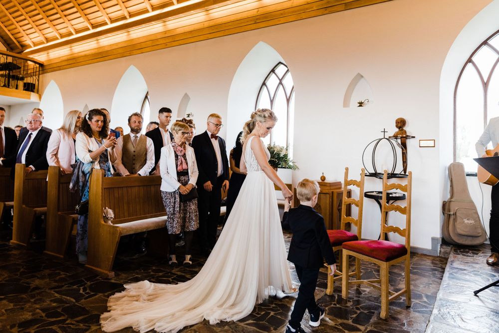 Wedding guests stand in church pews watching a special moment during the ceremony.