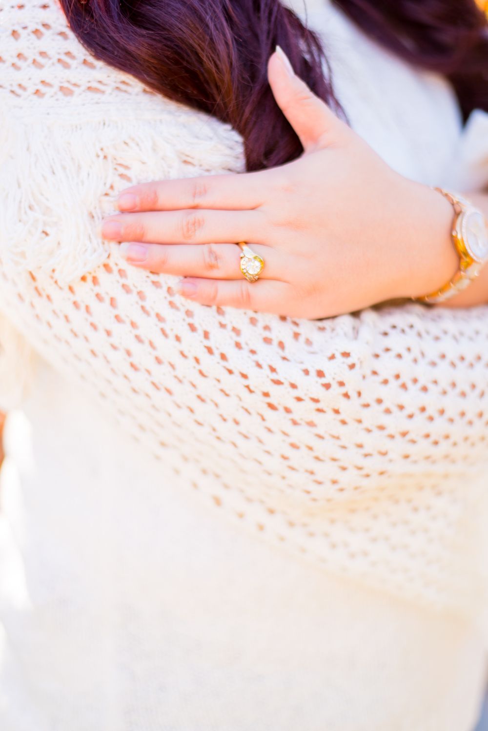 woman's hand with an engagement ring touching her arm in a white knitted sweater