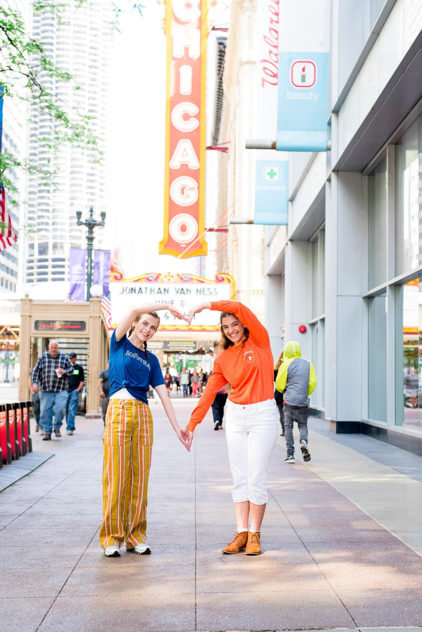 two senior girls in front of the Chicago Theater sign for Chicago senior pictures making a heart with their arms
