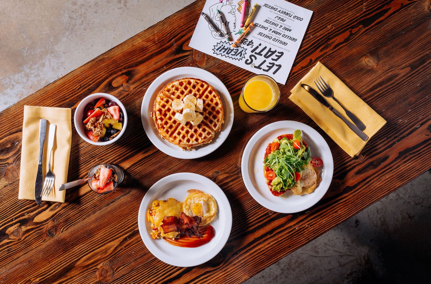 Overhead view of breakfast spread with waffles, eggs, and sides on wooden table.