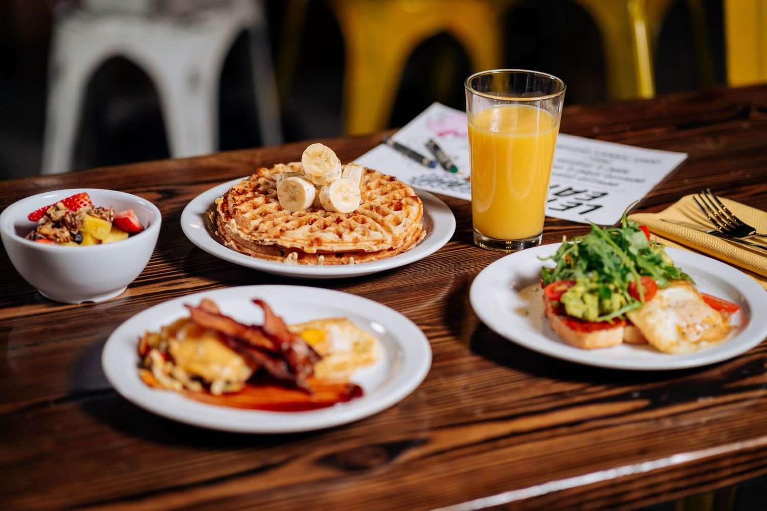 Breakfast spread featuring waffles, eggs, and orange juice on rustic wooden table.
