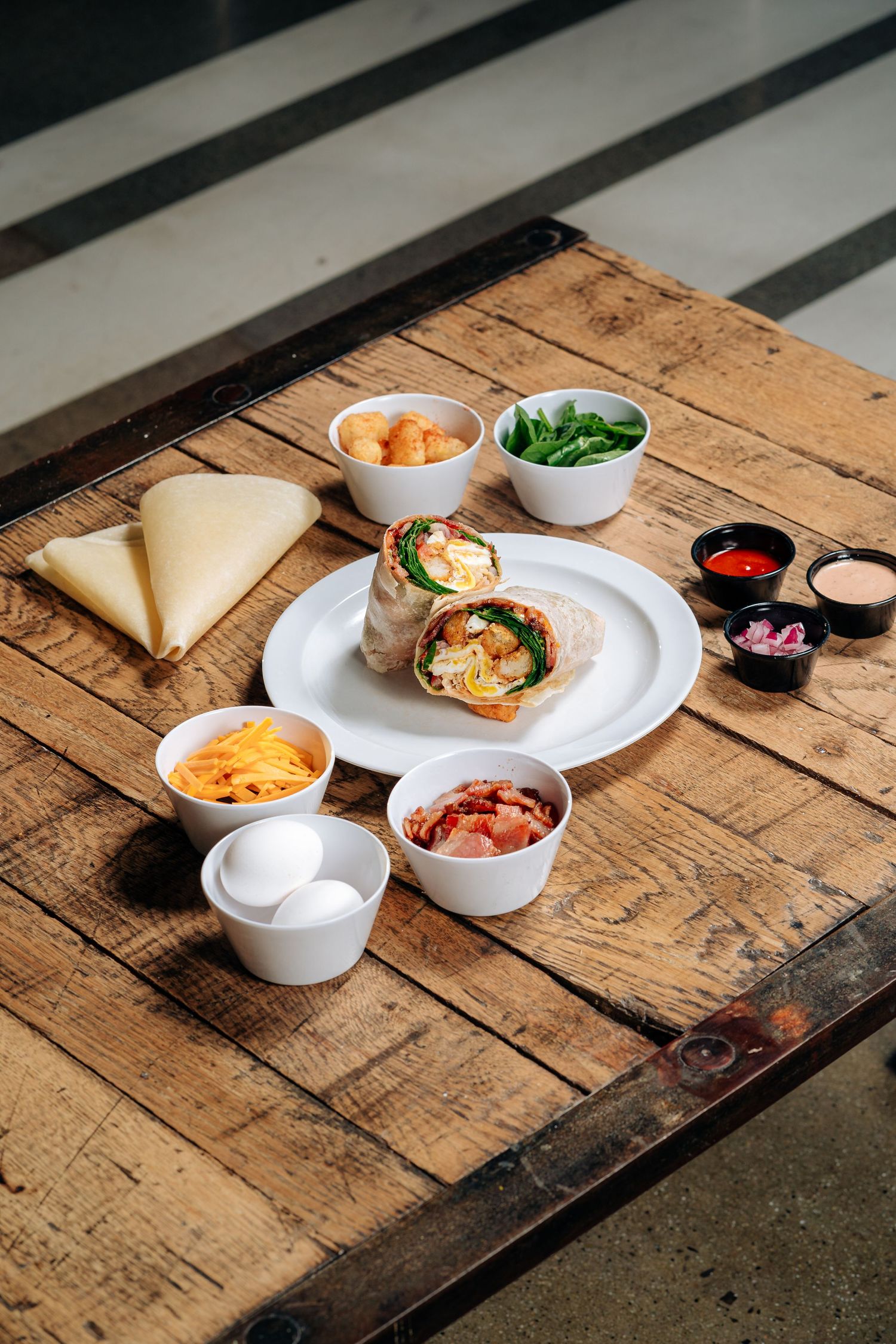 Gourmet wrap sandwich served on rustic wooden table with various condiments and side dishes.