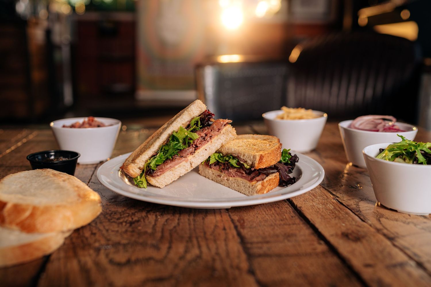 Sandwich plate with sides served on wooden table in cozy restaurant setting.