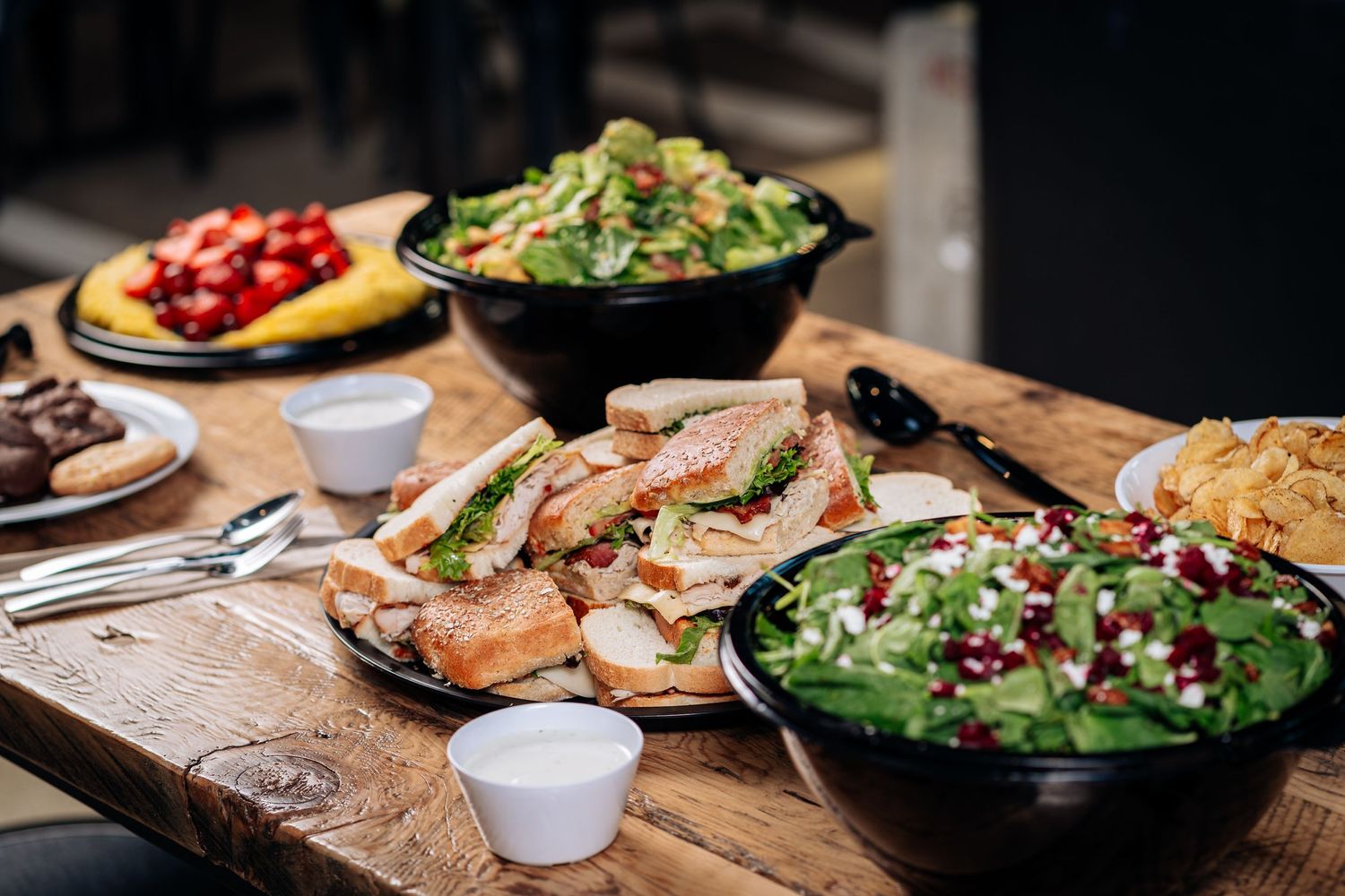 Fresh sandwiches and salads arranged on rustic wooden table with appetizers and garnishes.