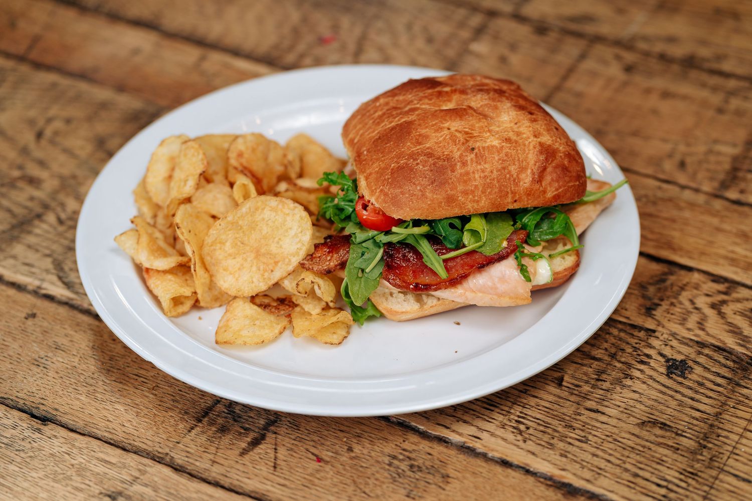 Classic sandwich served with potato chips on white plate atop wooden surface.