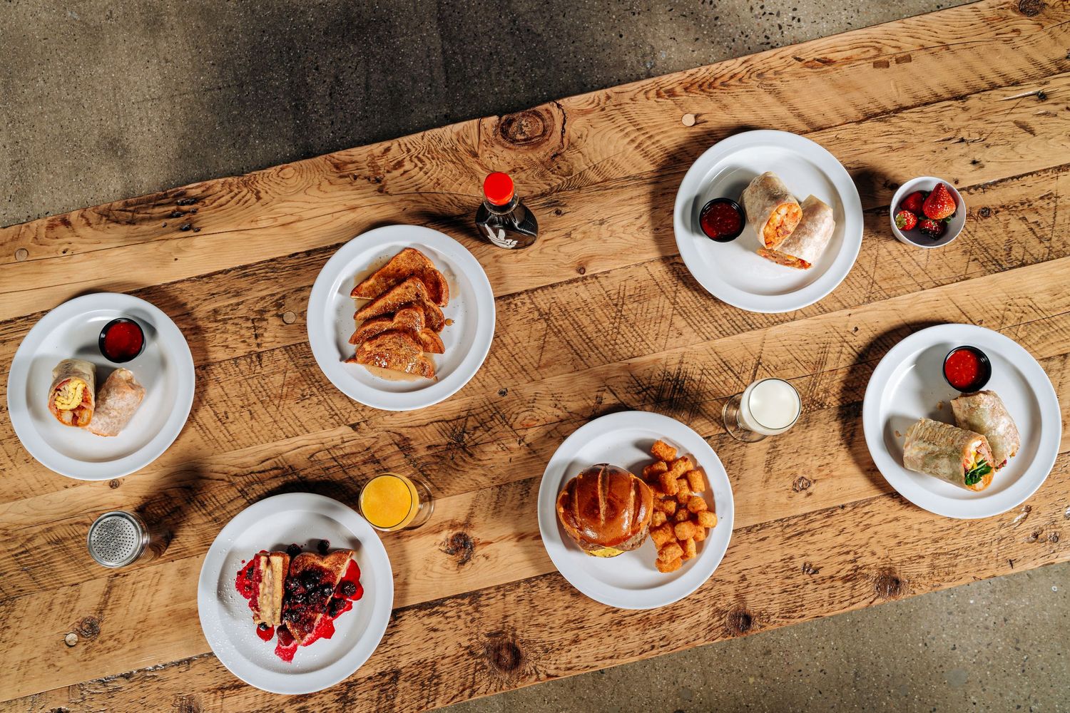 Overhead view of multiple breakfast plates arranged on rustic wooden table.