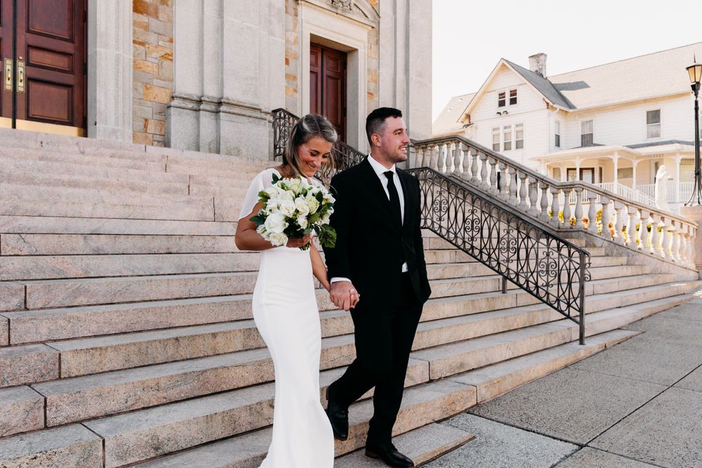 A couple descending stone church steps after their wedding ceremony holding a white bouquet.