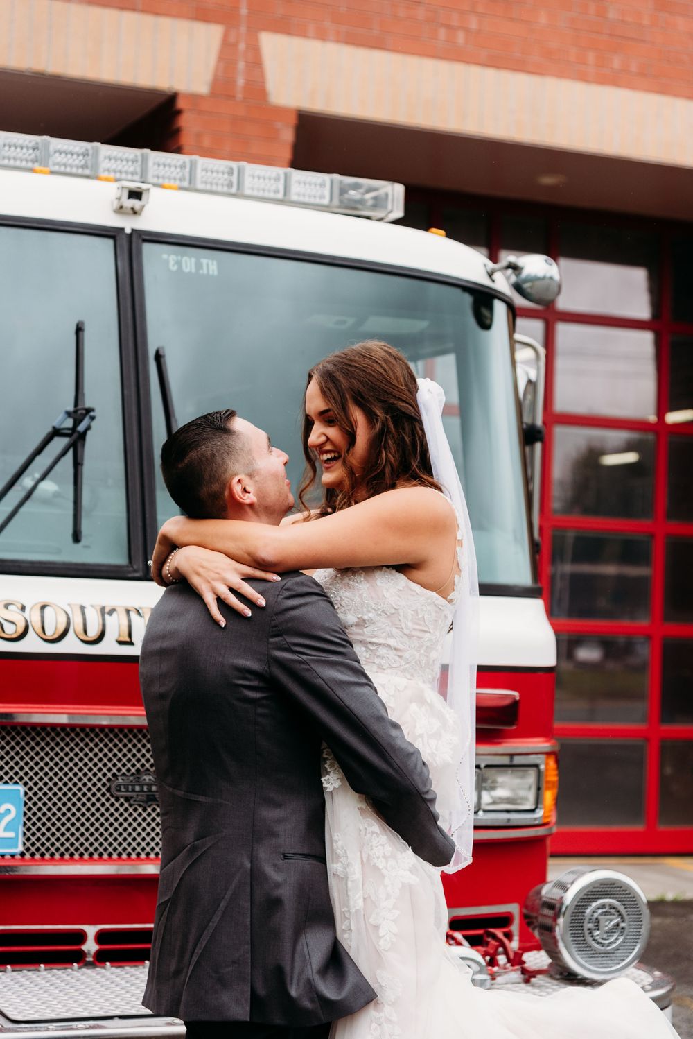A bride and groom share a joyful embrace in front of their fire truck.