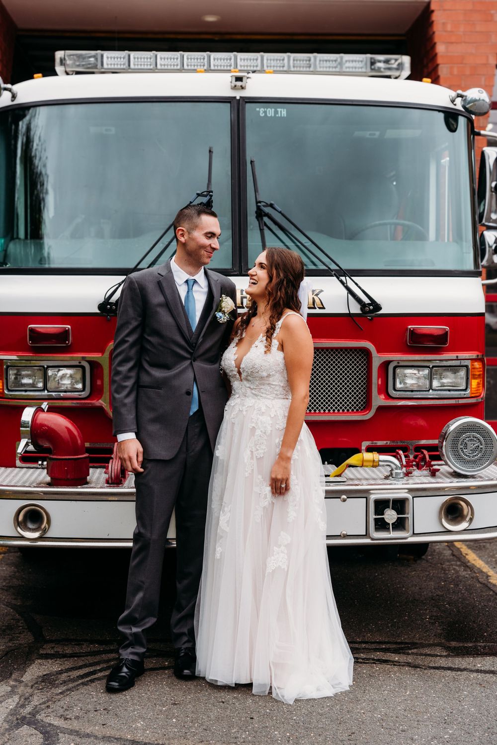 A couple in wedding attire poses in front of a red fire truck.