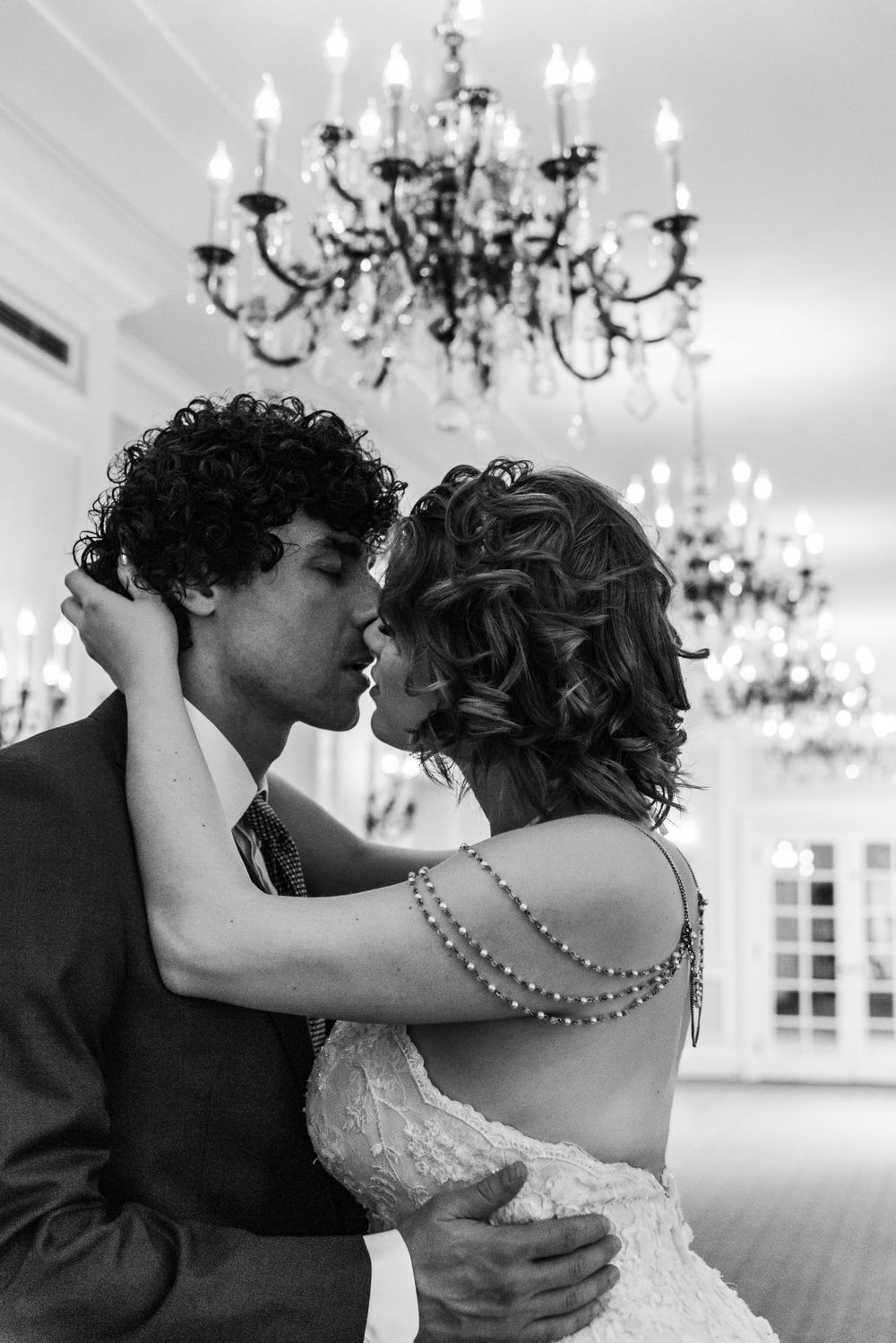 Romantic wedding couple shares an intimate moment under elegant crystal chandeliers in black and white photography.