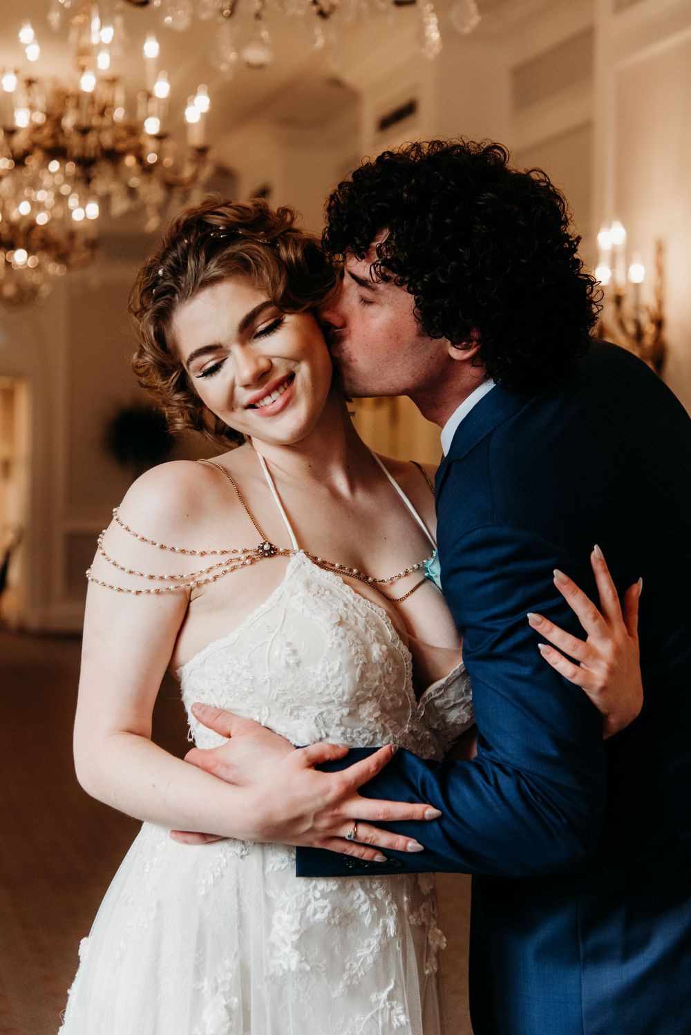Newlyweds share a tender moment under chandeliers during their wedding celebration.