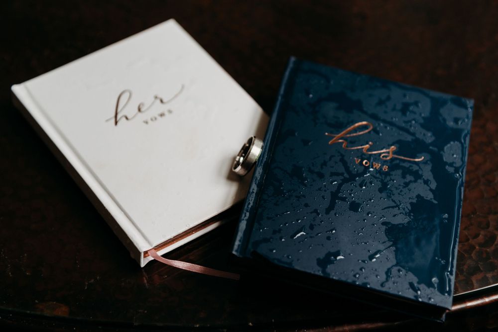 Two wedding vow books, one white and one navy blue, resting on a dark wooden surface.
