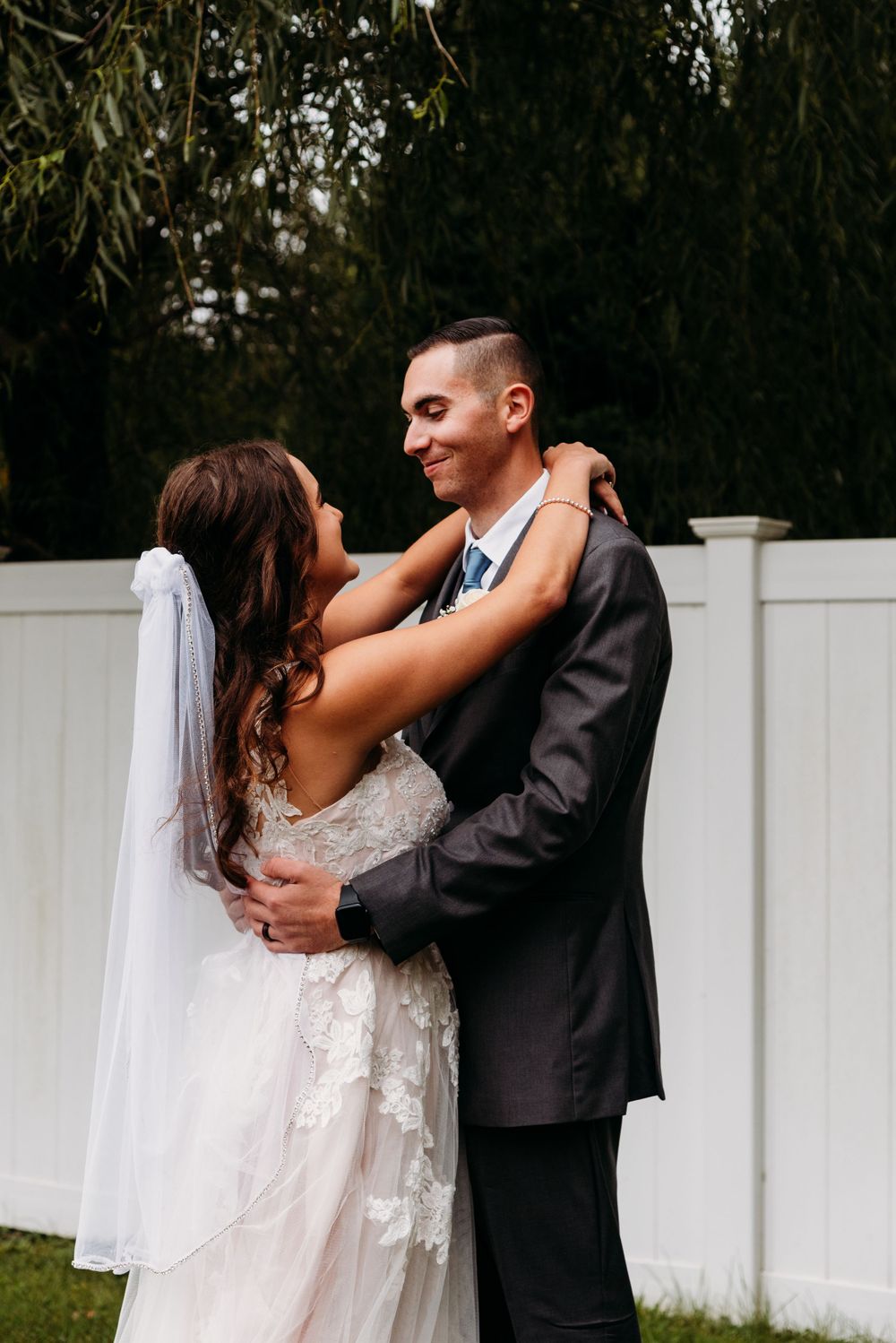 A couple shares an intimate moment against a white fence backdrop.