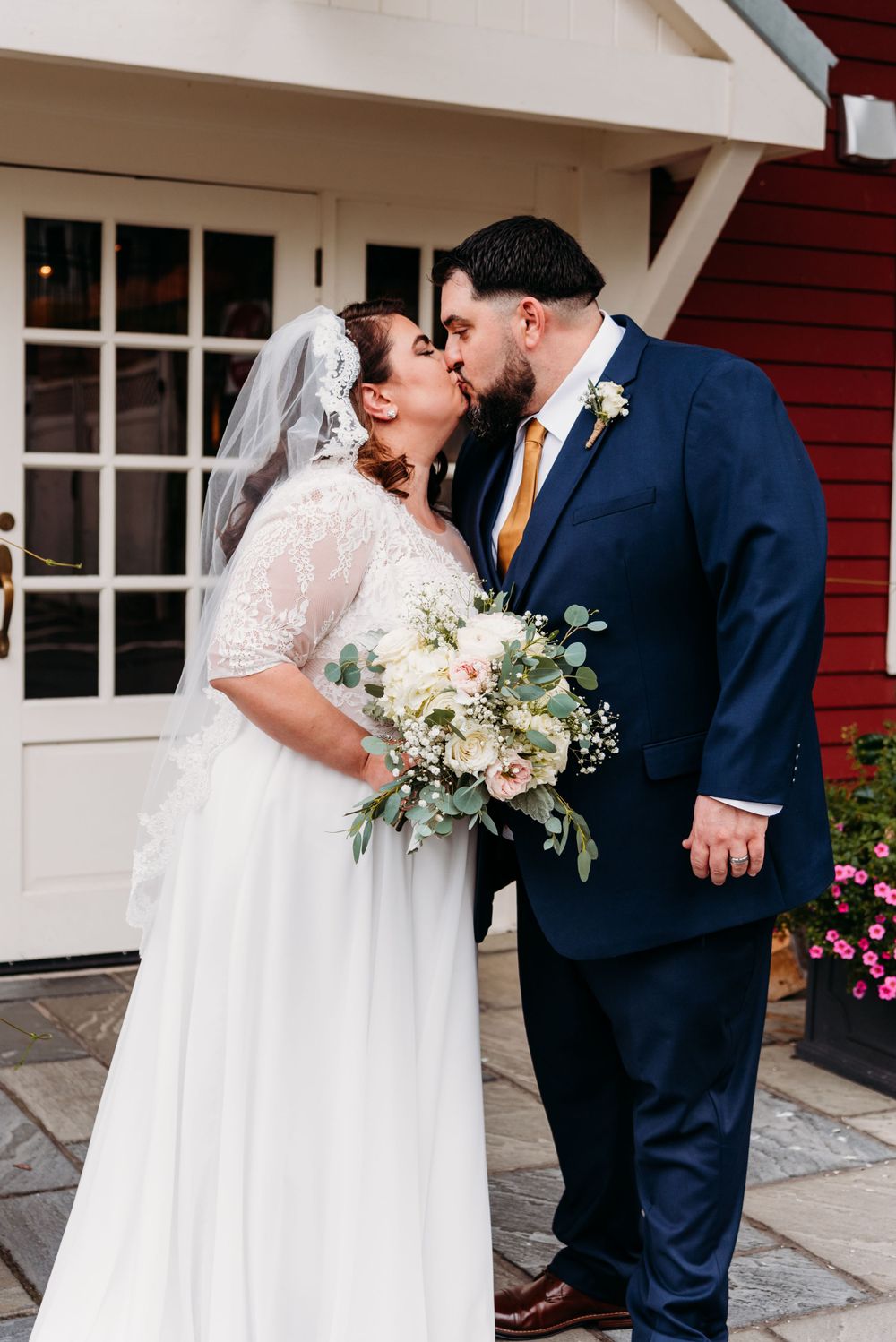 Newlywed couple shares romantic kiss outside red building.