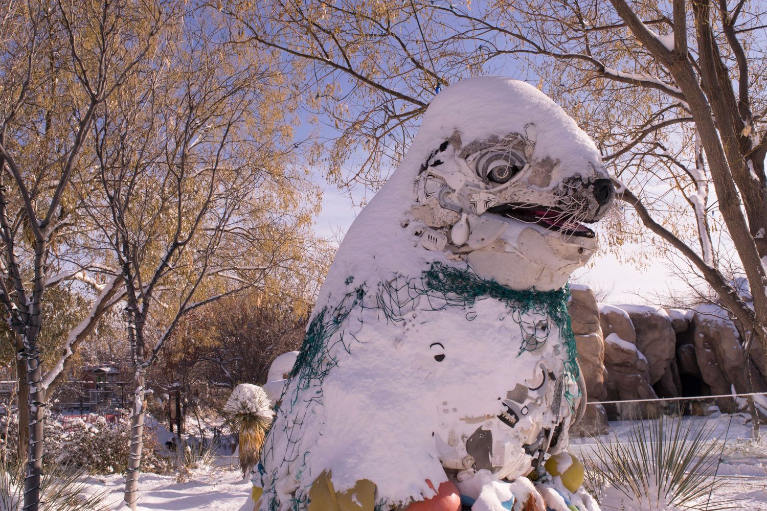 A large snow-covered bird sculpture stands among bare winter trees in a snowy landscape.