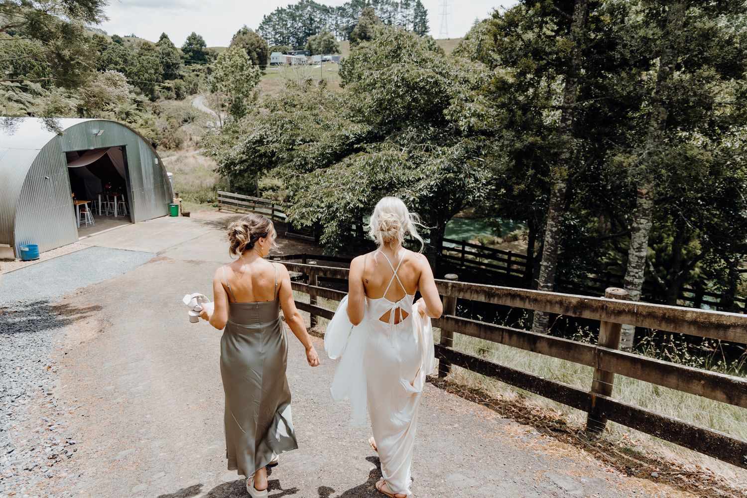 Two people walking down a gravel path with a quonset hut visible in the background.