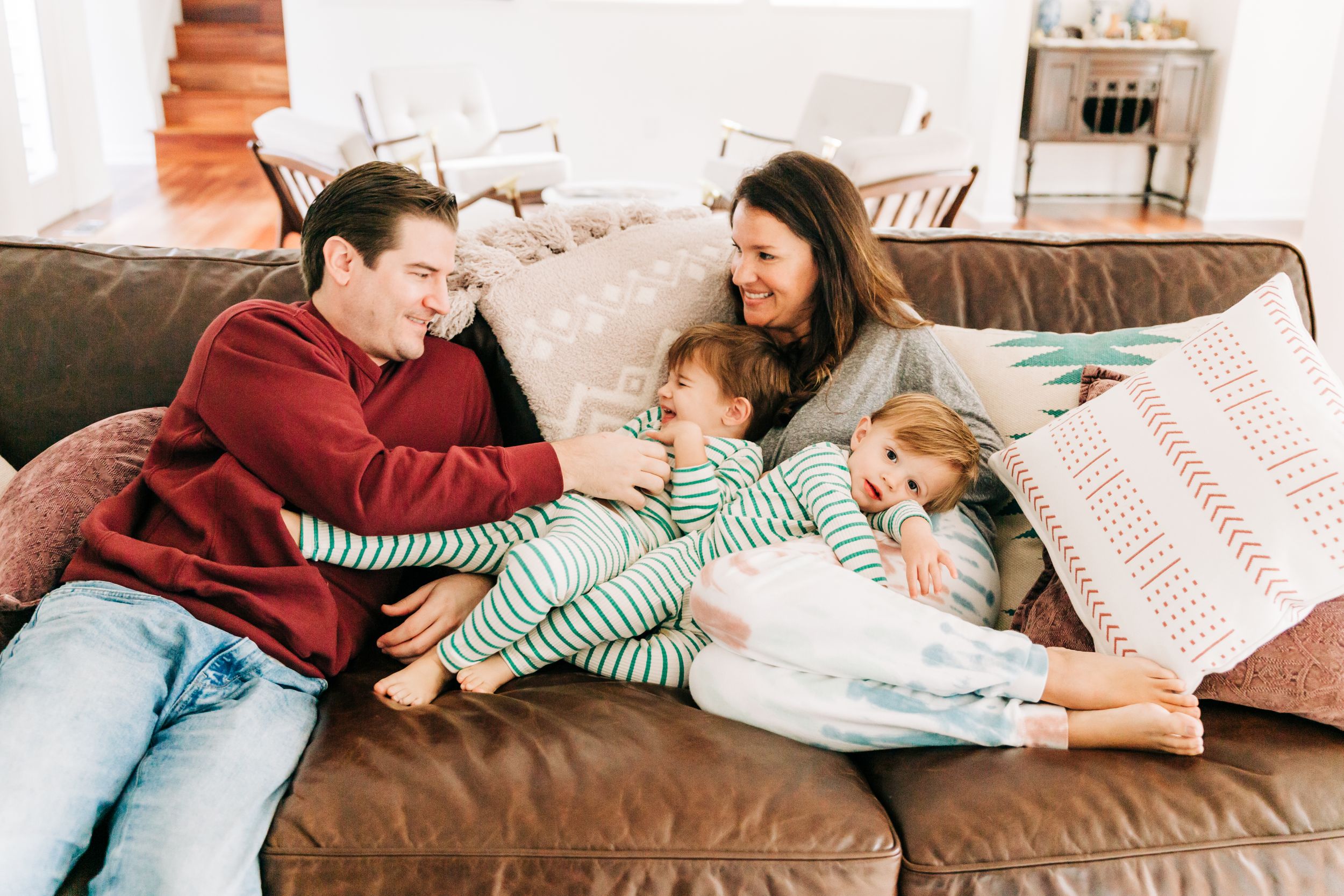 Family sitting on the couch. Dad tickles his son and mom is laughing