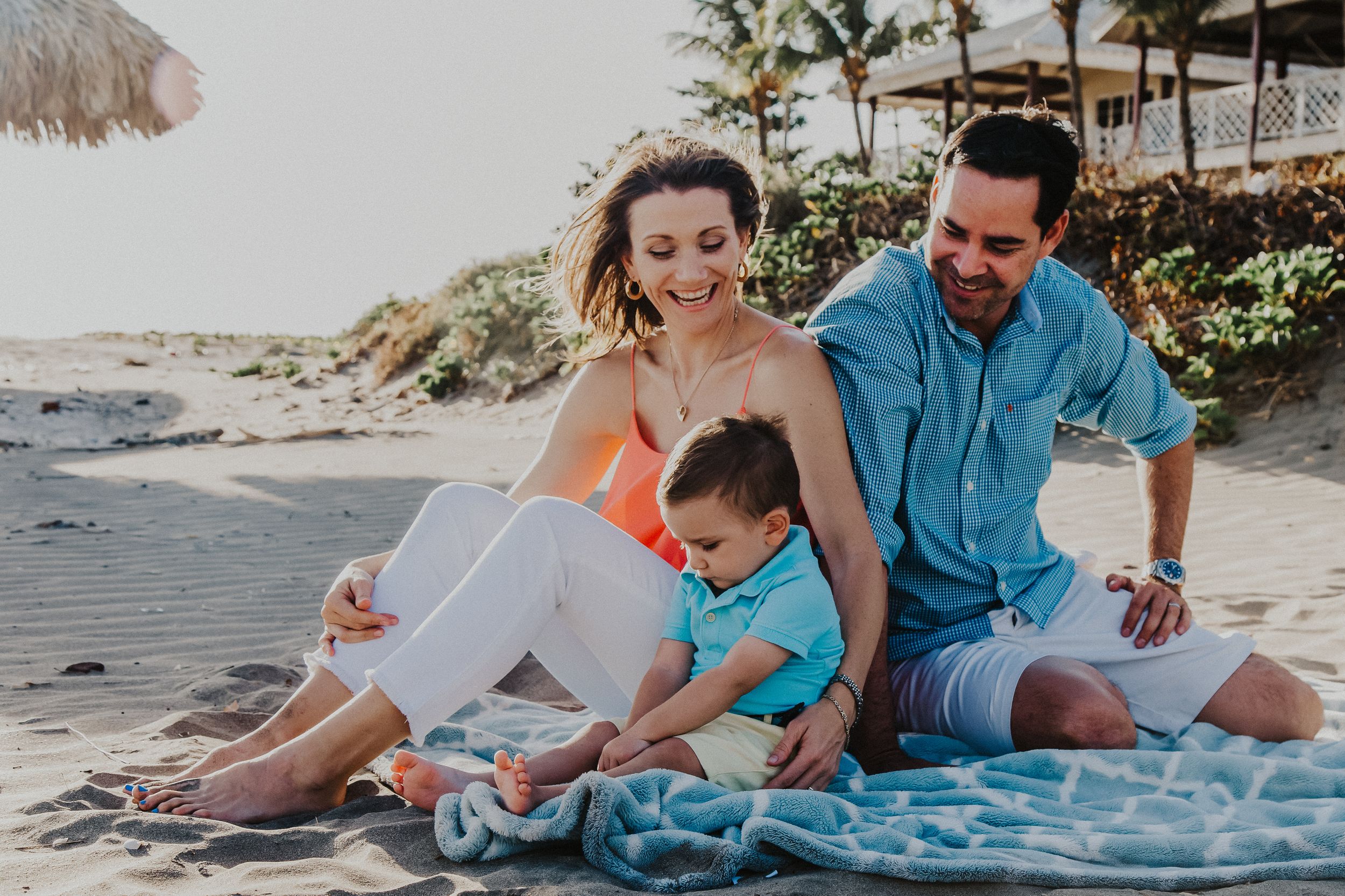 family of three sit happily on the beach