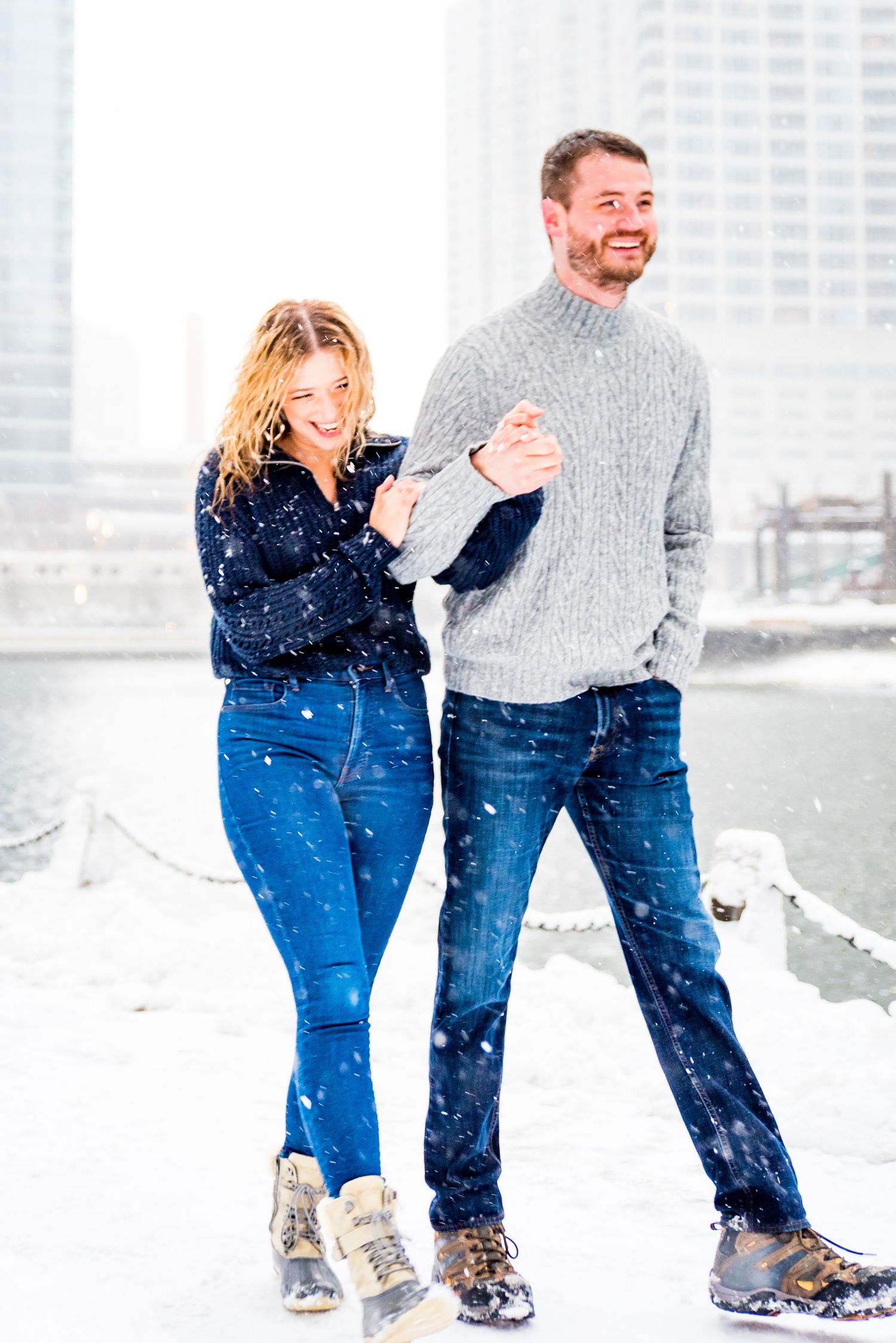 man and woman in navy and grey sweaters smiling in snow at Wolf Point Chicago