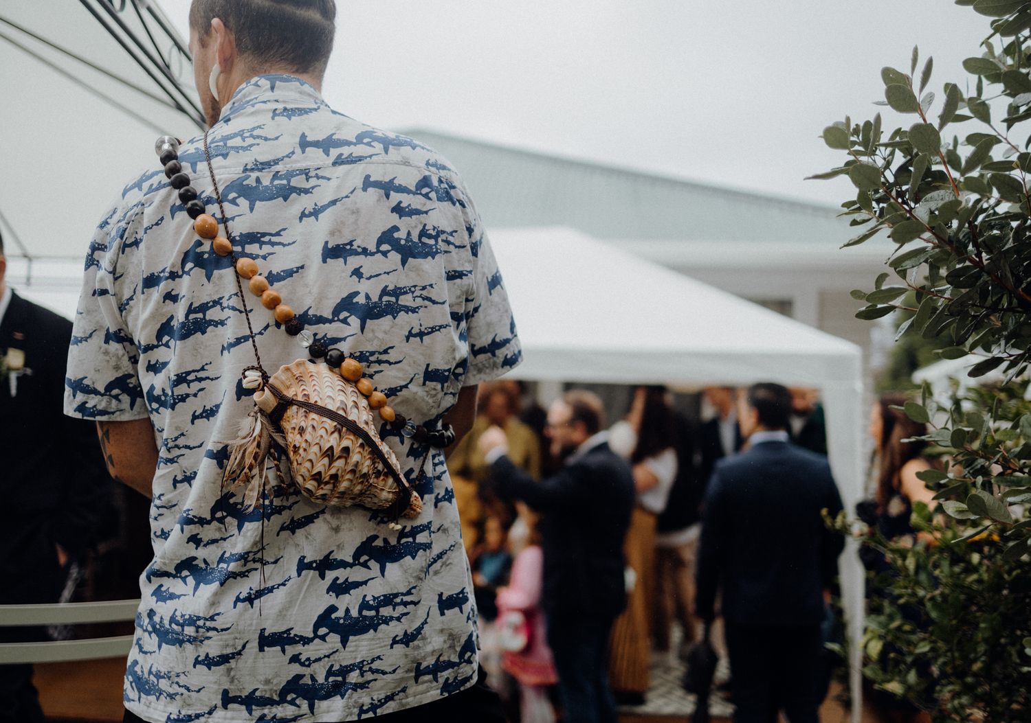 Guest in patterned shirt at outdoor wedding reception under white tent.
