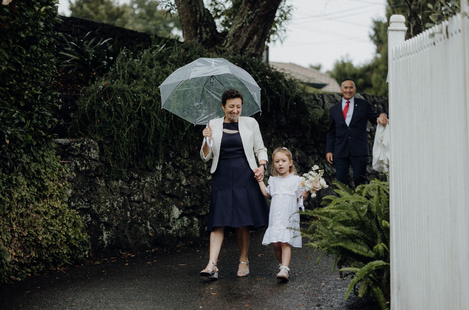 A rainy day outdoor scene with people walking under a clear umbrella.