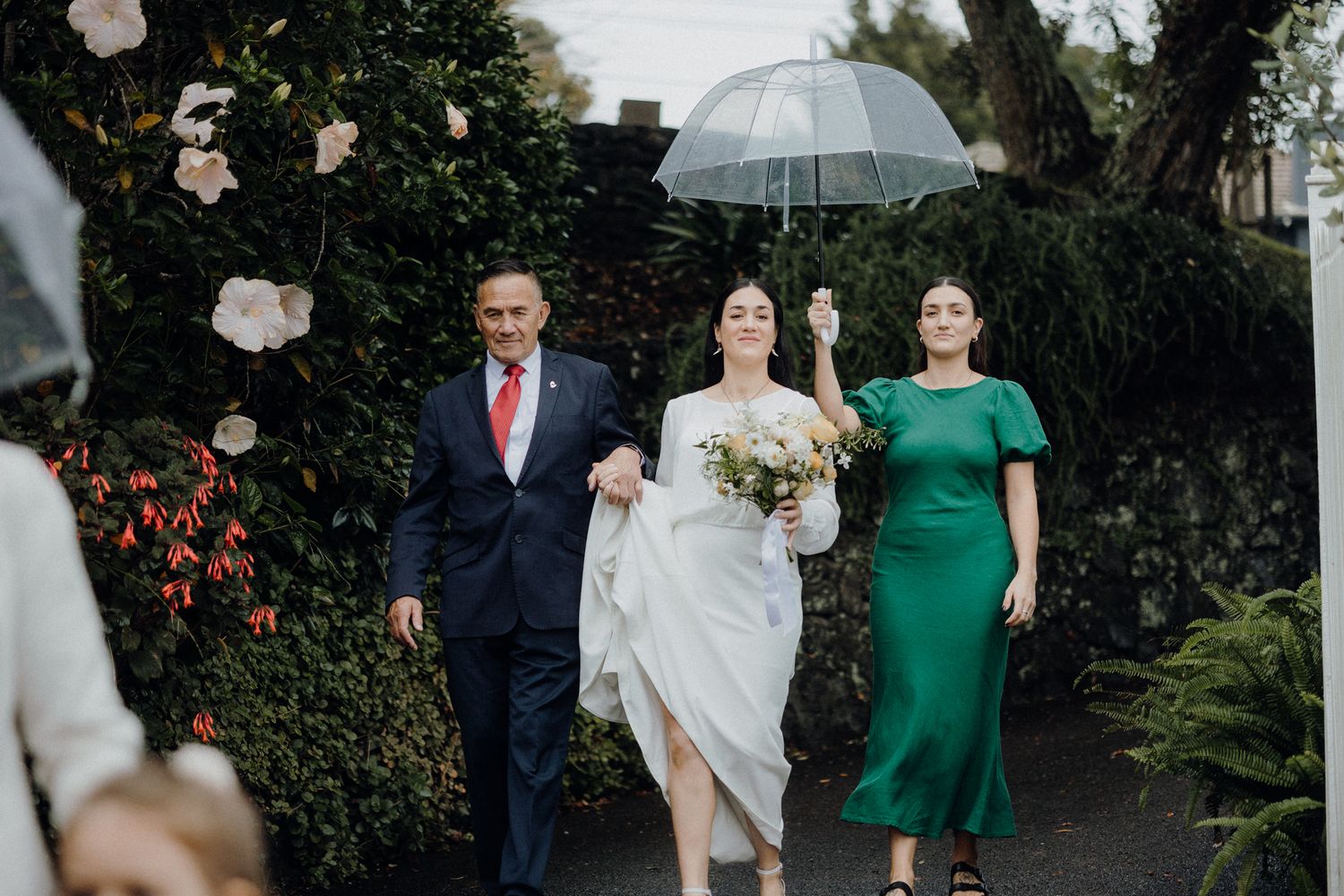 A wedding party walking down a garden path with vibrant floral surroundings.