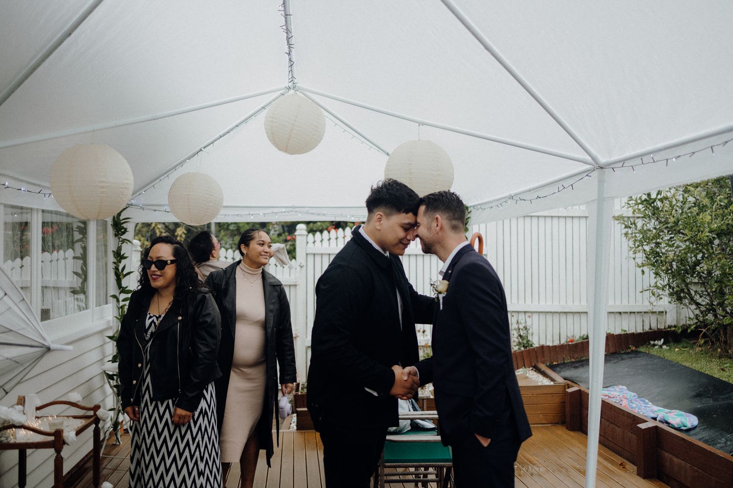 Wedding guests and couple gather under an elegant white tent during a daytime celebration.