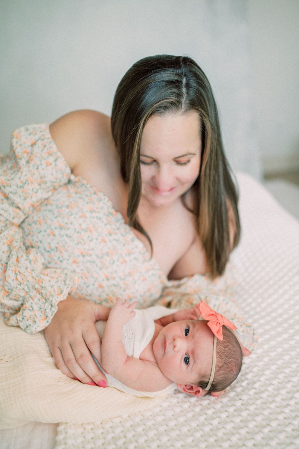 Tender newborn photography session with parent and baby on white textured bedding.