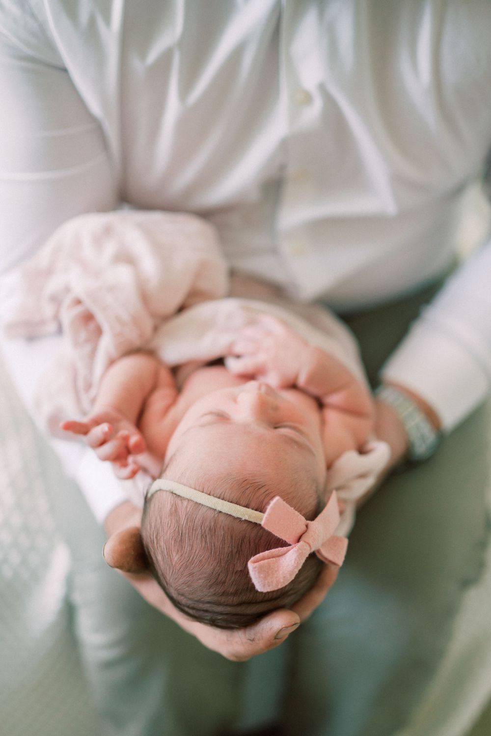 Close-up of baby with pink bow headband being cradled in white clothing.