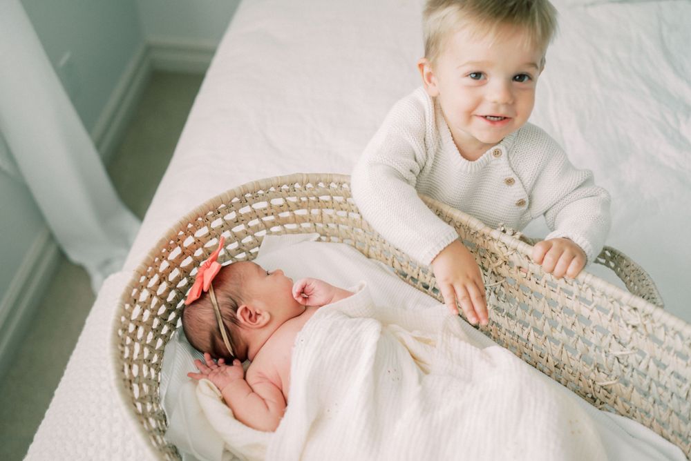A newborn baby rests in a woven bassinet while being watched from above.