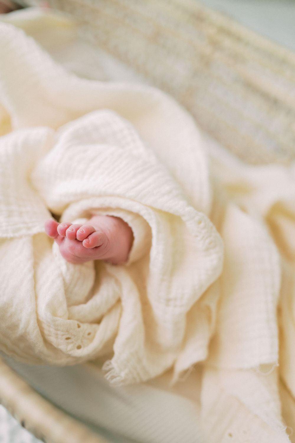A tiny baby foot peeks out from soft cream-colored blanket folds.