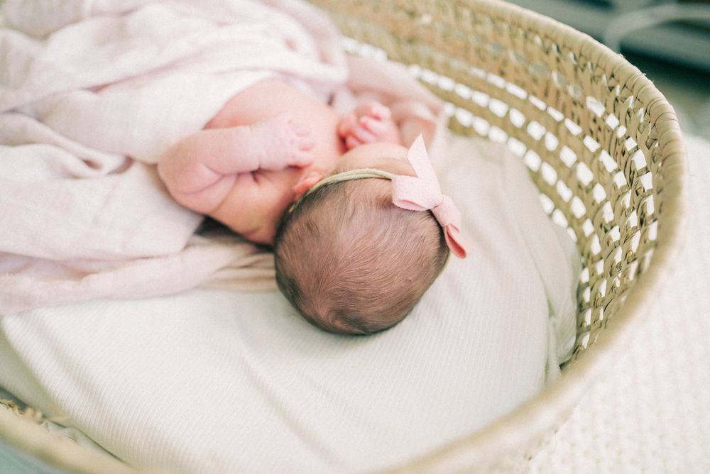 Sleeping newborn wrapped in soft white blanket in woven basket.