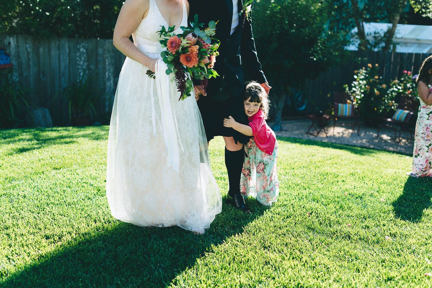 Little girl hugging grooms leg after their wedding ceremony