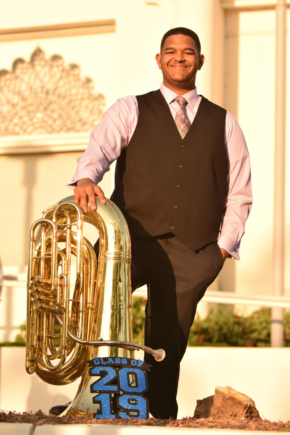 Musician in formal attire poses with tuba next to 2019 decoration.
