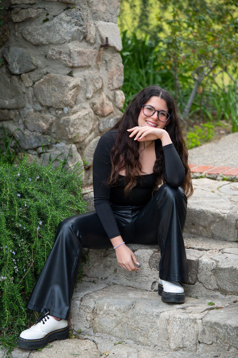 Person in black outfit sitting on stone steps in garden setting.