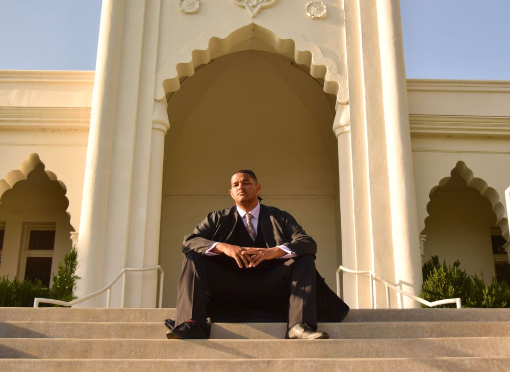 Graduate sits on ornate stone steps under an arched entryway.