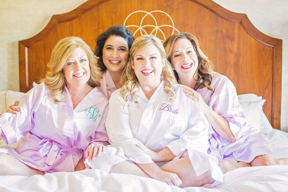 Bride with bridesmaids in robes on bed at Allegretto Vineyard Resort