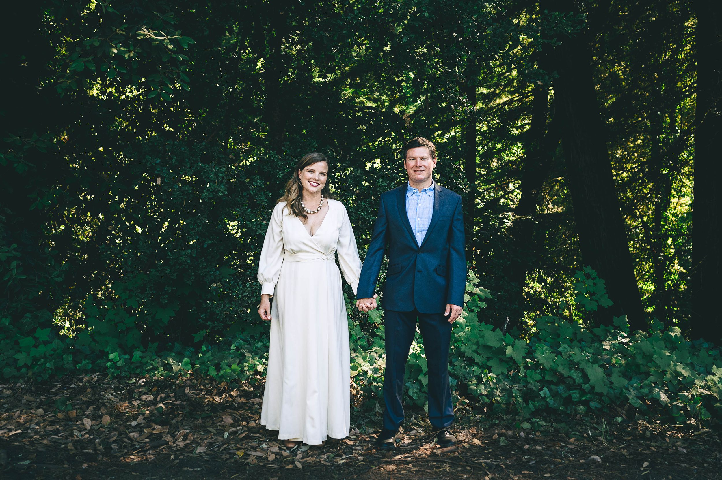 Bride in long sleeve wedding dress and groom in blue suit with redwood trees in the background.